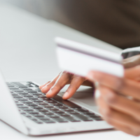 one hand typing on a keyboard and one hand holding a credit card